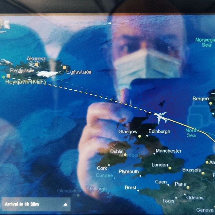 Joschi mit Maske spiegelt sich im Entertainment-Bilddchirm des Flugzeugs. Dieser zeigt Island auf der Karte.