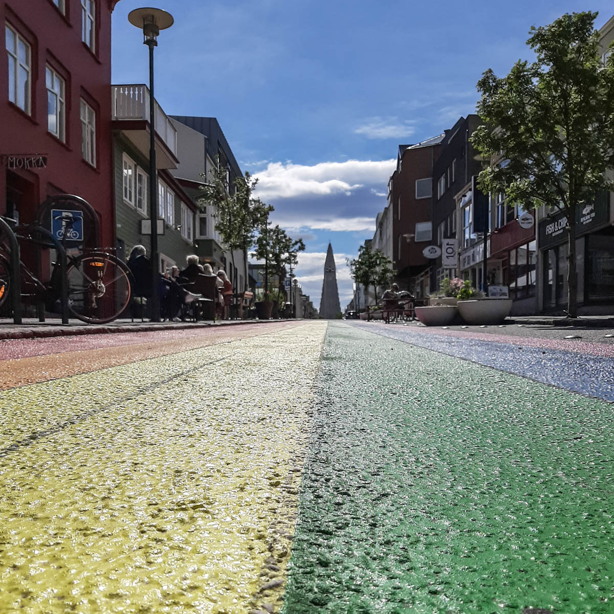Blick von der Straße auf die Hallgrímskirkja in Reykjavík. Die Straße ist in Regenbogenfarben gestrichen.