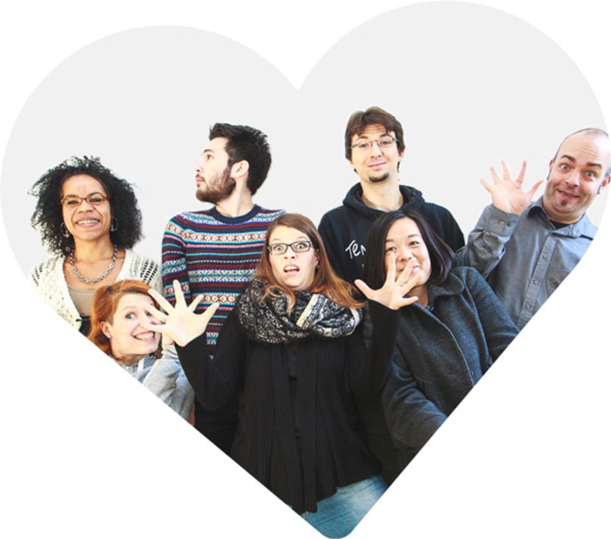 Das Tollwerk-Team vor einer hellgrauen Wand in einer albernen Pose. Einige schneiden Grimassen oder gestikulieren mit den Händen. Das Foto ist herzförmig beschnitten.