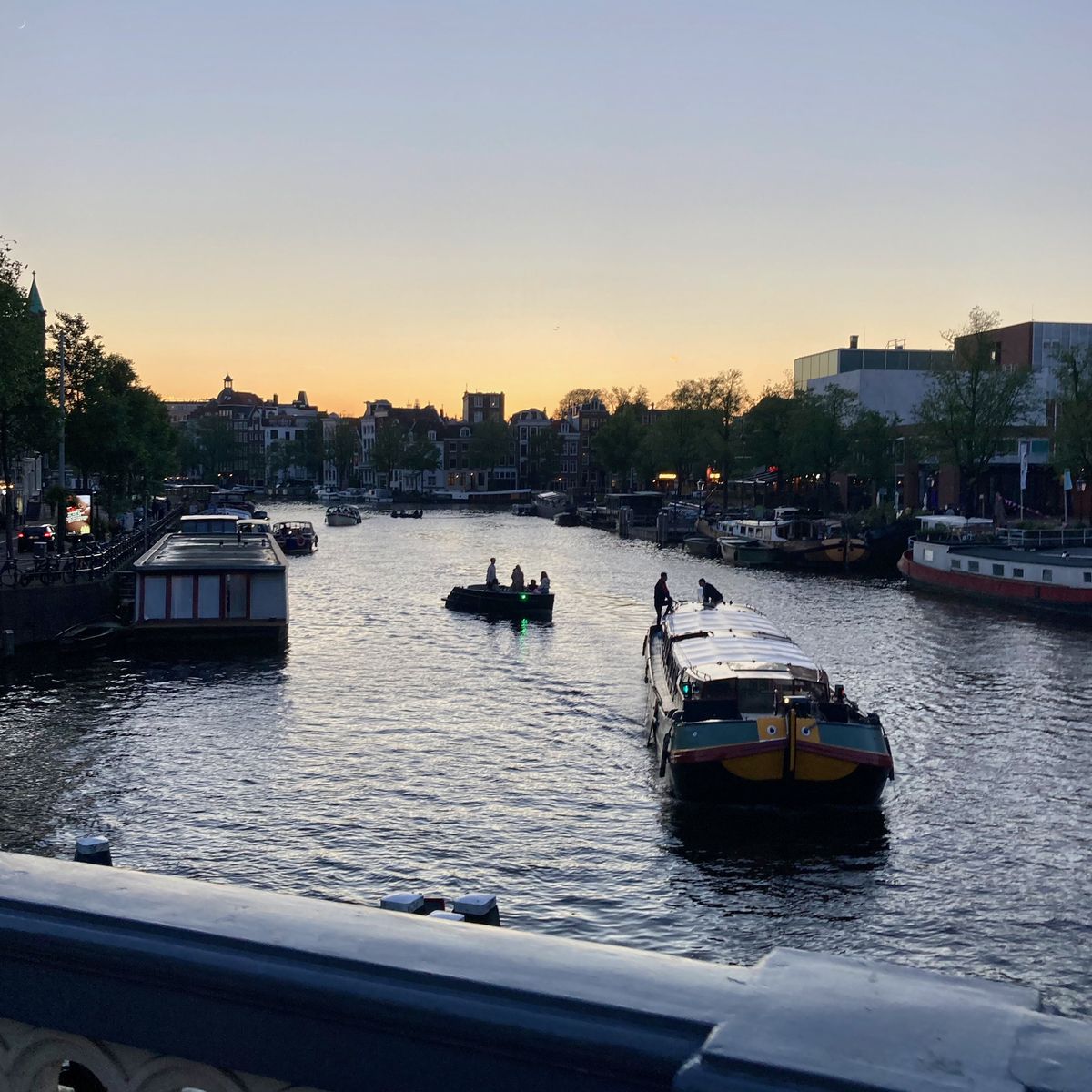 Blick auf eine der mit Booten befahrenen Grachten von Amsterdam bei Sonnenuntergang