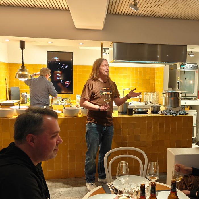 Marc begrüßt die Gäste. Hinter ihm die offene Küche mit arbeitendem Koch.