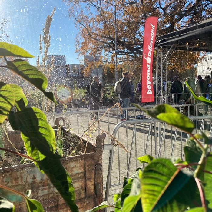 Rote Beyond Tellerrand Fahne mit weißem Schriftzug, Teilnehmende, durch ein Fenster aufgenommen