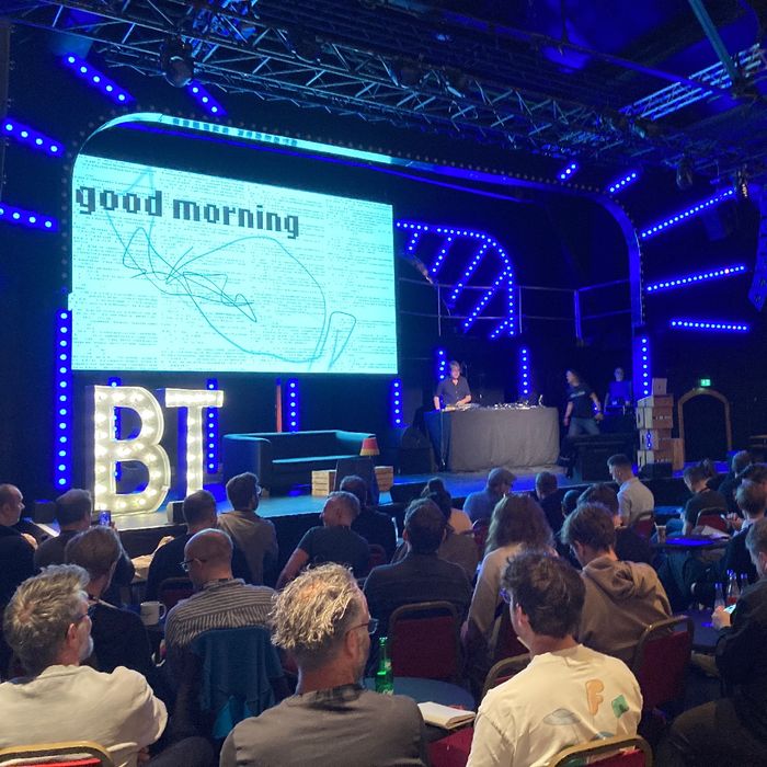 Blick in Richtung Bühne eines Veranstaltungssaals. Projektiert ist „Good Morning“