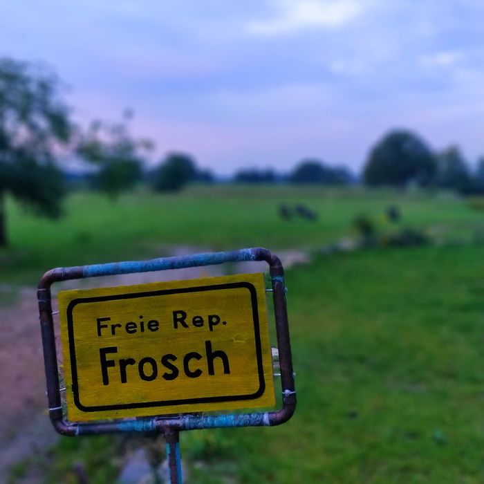 Gelbes Verkehrsschild mit der Aufschrift "Freie Rep. Frosch" am Rande der Felder neben dem Hof