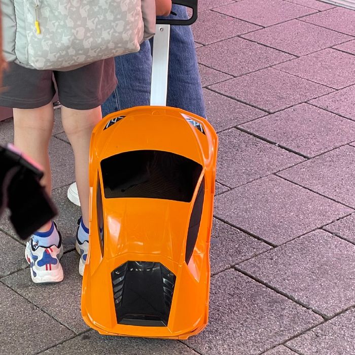 Ein Kind mit einem wirklich coolen Koffer in Form eines orangenen Rennwagens.