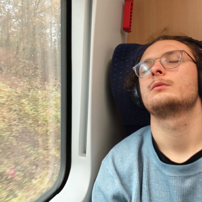 Jakob döst mit geschlossenen Augen und Kopfhörern im Zug vor sich hin.