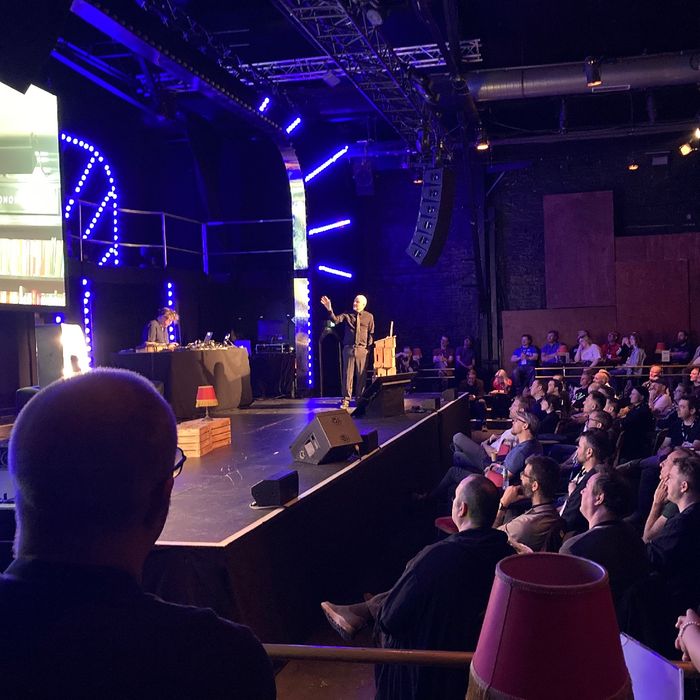 Redner auf einer Bühne, Publikum hört gebannt zu