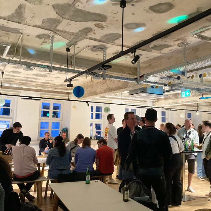 Blick in einen Raum, in dem viele Nenschen zusammenstehen, ein Getränk in der Hand, sich unterhaltend