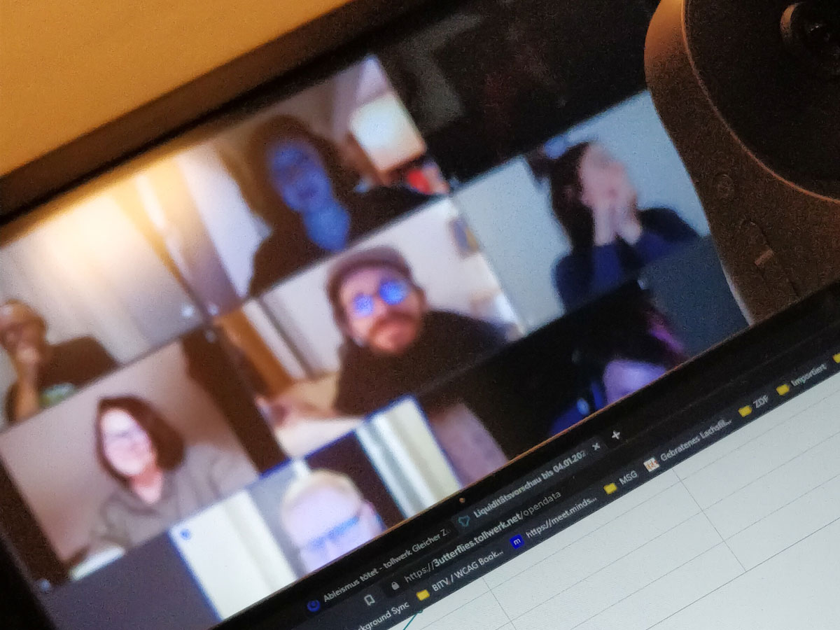 Im Vordergrund der Ausschnitt eines Laptop-Bildschirms, darauf sichtbar ein Browser-Tab mit dem Titel „#AbleismusTötet“. Im Hintergrund ein Bildschirm mit den unscharfen Avataren eines Zoom-Calls, in der Mitte Raúl Krauthausen.