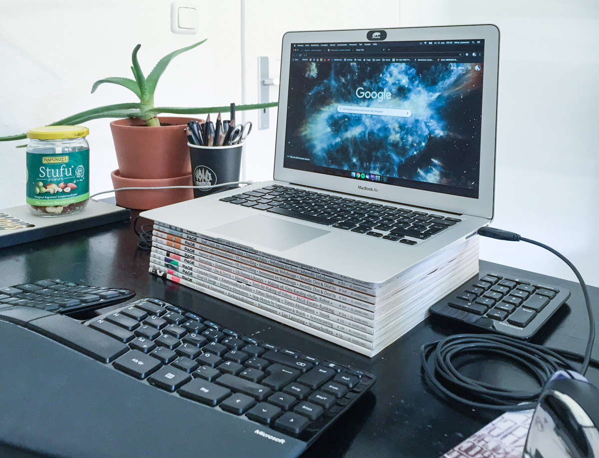 Laptop auf einem Stapel PAGE-Zeitschriften, Tastatur und andere Schreibtisutensilien
