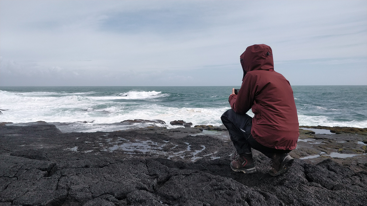 Nina kniet auf einem Felsen, um das Meer zu fotografieren