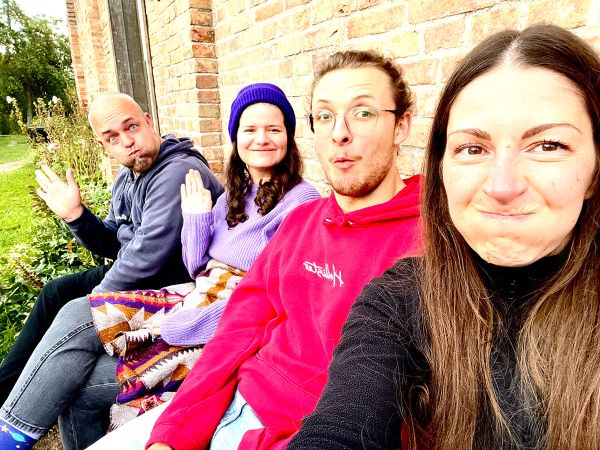 Angie, Jakob, Sophie und Joschi sitzen draußen auf einer Bank und machen verschiedene Grimassen. Angie macht das Selfie. 